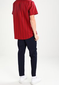 Rode kortemouwen shirt met marineblauwe verticale strepen, ronde zoom, gecombineerd met marineblauwe broek en witte sneakers. Gladde stof textuur.