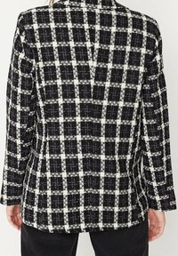 Mustavalkoinen ruudullinen bleiseri, jossa on teksturoitu kangas, pitkät hihat ja takana halkio. Kuosi koostuu neliöistä ja ristiakenteista.