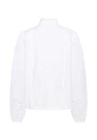Blouse blanche à manches longues avec un col montant, ornée d'accents en dentelle texturée sur les manches et sur les côtés, fabriquée en tissu léger.