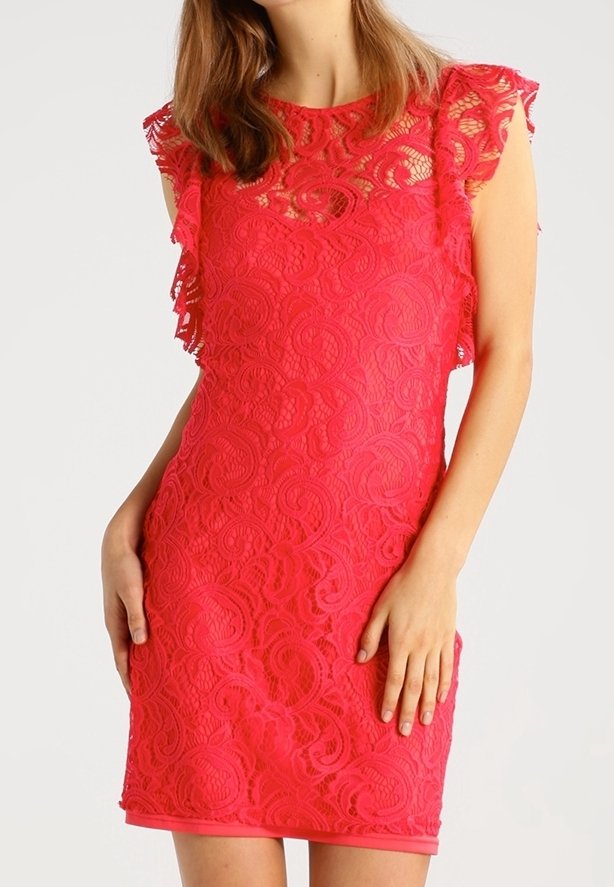 Femme portant une robe sans manches en dentelle rouge vif à motifs floraux, debout avec une main sur la hanche et l'autre détendue le long du corps.