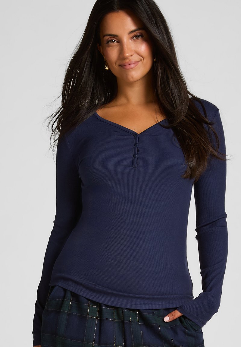 Marineblauw langslieve shirt met een geribbelde textuur, voorzien van een V-hals en drie donkere knopen aan de voorkant, gecombineerd met een geruite rok.
