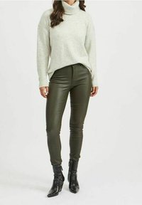 Vaaleanharmaa, korkean kauluksen villapaita yhdistettynä tummanvihreisiin, istuviin housuihin ja mustiin nilkkasaappaisiin. Villapaidassa on rento malli ja ribbiä.