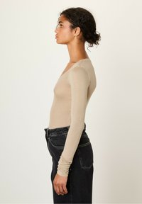 Beige long-sleeve top with a low neckline, fitted design, and ribbed texture, paired with high-waisted dark denim jeans.