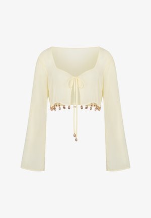 Cremfarbene, langärmlige, verkürzte Bluse mit vorderem Knoten und dekorativen goldenen Muschel-Anhängern am Saum.