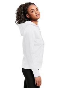 Vit hoodie med en framfickan i kängurustil, justerbar dragsko, ribbade ärmslut och en mjuk textur, bärs med svarta leggings.