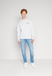 Sudadera gris claro con puños y dobladillo acanalados, con el logo "TOMMY JEANS". Combinada con jeans azul claros y zapatillas blancas.