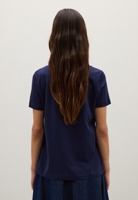T-shirt blu navy a maniche corte in cotone, con vestibilità comoda e scollatura rotonda, visto da dietro con lunghi capelli mossi visibili.