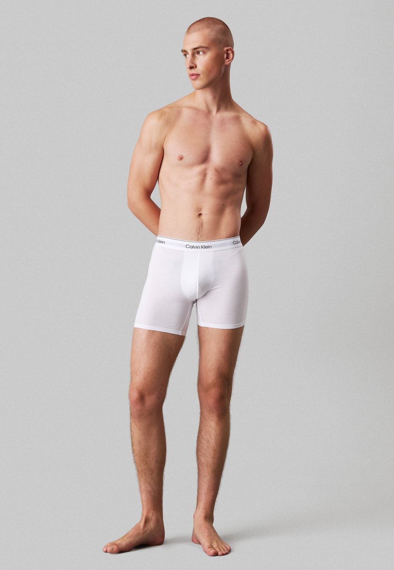 Fehér pamut boxer alsónadrág elasztikus derékrésszel, amelyen a Calvin Klein logó található. Sima textúrájú és testhez simuló dizájn, térdhosszig.