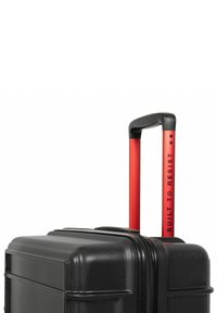Černý tvrdý kufr s texturovaným povrchem a černými zipy. Telescopická rukojeť v červené barvě s potiskem "BUILT TO RESIST". Pevná konstrukce.