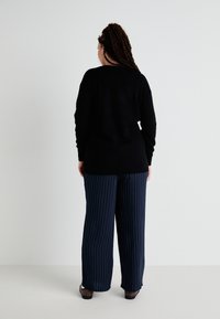 Sweater preto de mangas longas, combinado com calças largas azul-marinho com riscas brancas verticais. Textura suave com um corte descontraído.