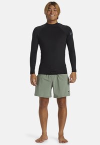Rash guard negro de manga larga y pantalones de baño verde claro. Tejido suave con un diseño ajustado, que incluye un pequeño logo en el hombro.