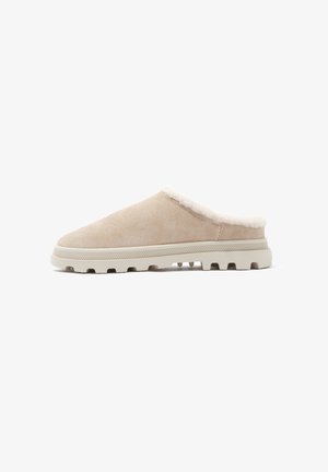 Beige Wildleder-Slipper mit weißem, flauschigem Futter und einer strukturierten Gummisohle mit Rillen für besseren Halt. Offenes Rückendesign.