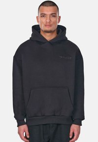 Black hoodie made of soft fabric with a front pocket, ribbed cuffs, and waistband. Features embossed logo on the chest. Loose fit.
