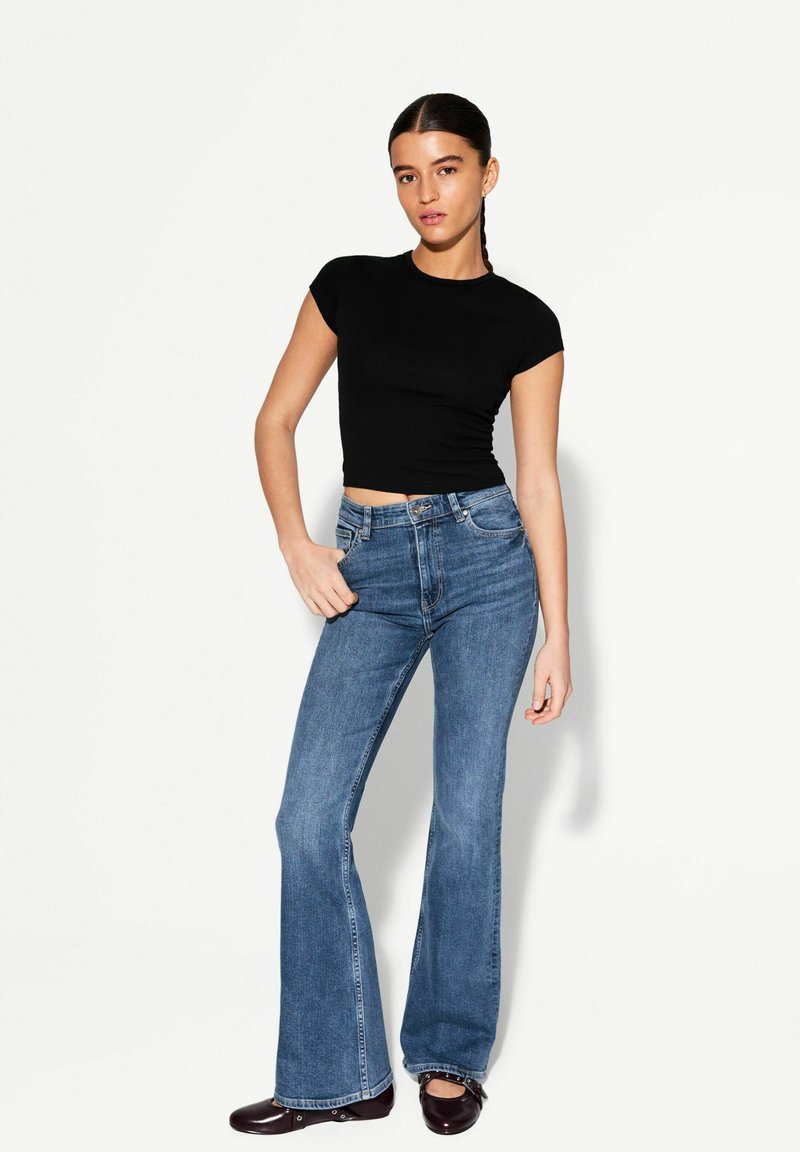 Schwarzes, kurzes T-Shirt mit kurzen Ärmeln, kombiniert mit hellblauen Schlagjeans. Die Jeans haben ein klassisches Fünf-Taschen-Design und feine Nähte.