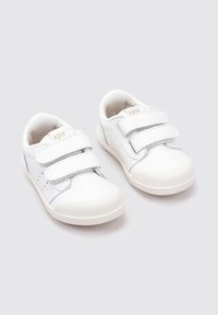 Zapatillas blancas con dos correas de Velcro, detalles en plata, interior texturizado y suelas de goma. Diseño minimalista con lados ventilados.
