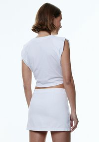 Witte cropped top met kapmouwen, gecombineerd met een witte minirok. Glad stof, eenvoudig ontwerp, strakke lijnen, zonder zichtbare patronen of accenten.