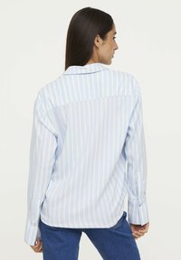 Light blue and white striped long-sleeve shirt, relaxed fit, features a back yoke and button cuffs, made from smooth fabric.