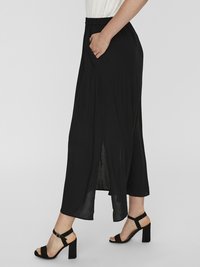 Jupe midi noire avec une taille élastique et des poches, en tissu fluide et avec une fente sur le côté, assortie à des sandales à talons noires.