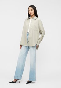 Ανοιχτό γκρι πουκάμισο σε υπερμεγέθη γραμμή με τσέπη στο στήθος, σε συνδυασμό με ανοιχτό μπλε ξεβαμμένο τζιν παντελόνι με φαρδιά μπατζάκια και μαύρες γόβες με μυτερή μύτη.