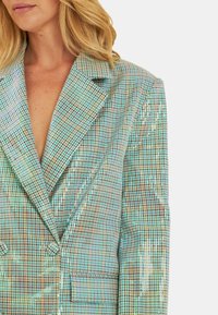 Blazer a quadri con paillettes in tonalità di azzurro chiaro, beige e verde. Presenta rever a percentuale e design doppiopetto con tasca frontale.