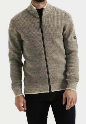 Cardigan zippé en tricot dans des tons beiges avec un motif texturé, col et poignets côtelés, équipé d'une fermeture éclair noire et d'un détail de logo subtil.