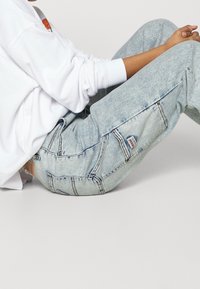 Ljusblå denimjeans med en urtvättad finish, som har flera fickor och sömdetaljer. Materialet verkar mjukt med en avslappnad passform.
