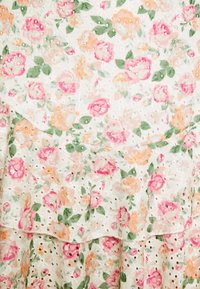 Robe fleurie avec un fond blanc, ornée de roses roses et pêches avec des feuilles vertes. Texture en œillets et design à volants superposés.