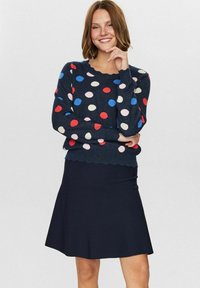 Mornarska pulover s pisano pikami, dolgi rokavi, rob z valovitim zaključkom; v paru s črno krilo s spuščenim krojem, gladka tekstura.