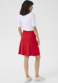 Jupe rouge en ligne A avec une taille élastique, faite d'un tissu lisse. Associée à un haut blanc ajusté et des baskets de couleur claire.