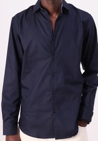 Navy blue long-sleeve shirt in cotton blend, featuring a pointed collar, front buttons, and a smooth texture with a fitted design.