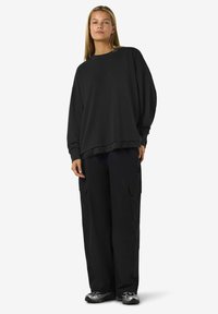 Felpa nera oversize con dettagli in pizzo all'orlo, abbinata a pantaloni cargo neri larghi e sneaker metalliche, caratterizzata da una silhouette rilassata.