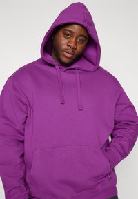Purple hooded sweatshirt with a front pocket, drawstring closure, and a soft, textured fabric. Features loose fit and stitched accents.