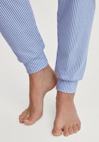 Blaue und weiße gestreifte Pyjamahosen mit elastischen Bündchen an den Knöcheln, aus weichem Baumwollmaterial. Barfußfüße im Vordergrund sichtbar.