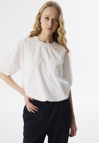 Witte, kortekorte top met een ronde halslijn en een klein, reliëfzakje. Gecombineerd met zwarte, nauwsluitende broek. Zachte textuur.