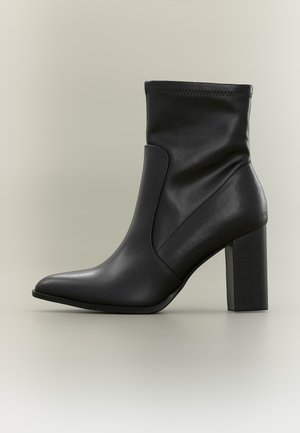 Bottine noire en cuir avec bout pointu et talon carré haut sur un fond neutre uni.