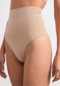 Shapewear beige a vita alta e senza cuciture. Texture liscia, copertura media, con un bordo a costine nella parte superiore. Progettato per comfort e supporto.