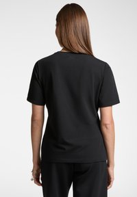 T-shirt nero a maniche corte realizzato in cotone morbido. Presenta un colletto rotondo e un piccolo dettaglio del logo sul retro, con una vestibilità rilassata.