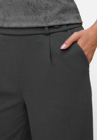 Ciemnoszare, dopasowane spodnie o gładkiej fakturze, z zapięciem na guzik i kieszeniami po bokach, zestawione z szarym, teksturowanym topem.