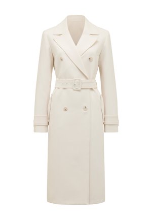 Trench-coat long en crème à double boutonnage avec larges revers, ceinture assortie, lanières aux poignets et poches latérales, présenté sur fond blanc.
