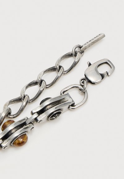 Chaîne argentée épaisse avec fermoir homard, étiquette Versace gravée et perles décoratives brunes intégrées dans des maillons en métal.