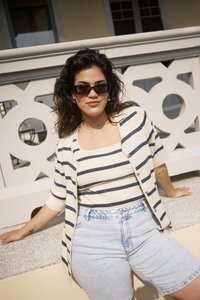 Cárdigan de punto a rayas en crema y marino, combinado con una blusa ajustada a juego y pantalones cortos de mezclilla de cintura alta. Los accesorios incluyen gafas de sol y un collar.