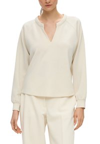 Lichtbeige pullover met een V-hals, raglanmouwen en geribbelde boorden. Gemaakt van zacht materiaal met een ontspannen pasvorm en een minimalistisch ontwerp.