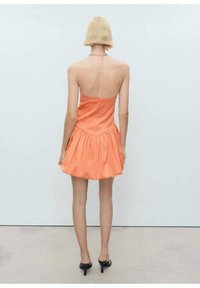 Rochie portocalie fără bretele, cu un corset ajustat și fustă evazată, plisată. Textură de țesătură netedă, închidere cu fermoar la spate și detaliu din lanț la gât.
