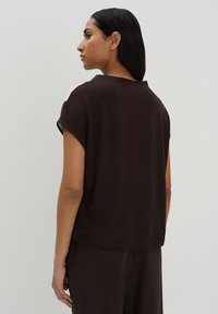 Top marrone a maniche corte con un fit rilassato e scollatura rotonda, caratterizzato da un dettaglio a contrasto sulle spalle. Tessuto liscio e leggero.