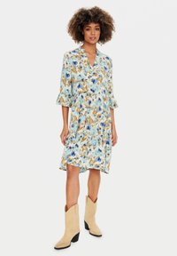 Rochie florală albastră cu mâneci trei sferturi, decolteu în V și un design în straturi. Purtați cu cizme cowboy maronii. Materialul este ușor și cu un model.