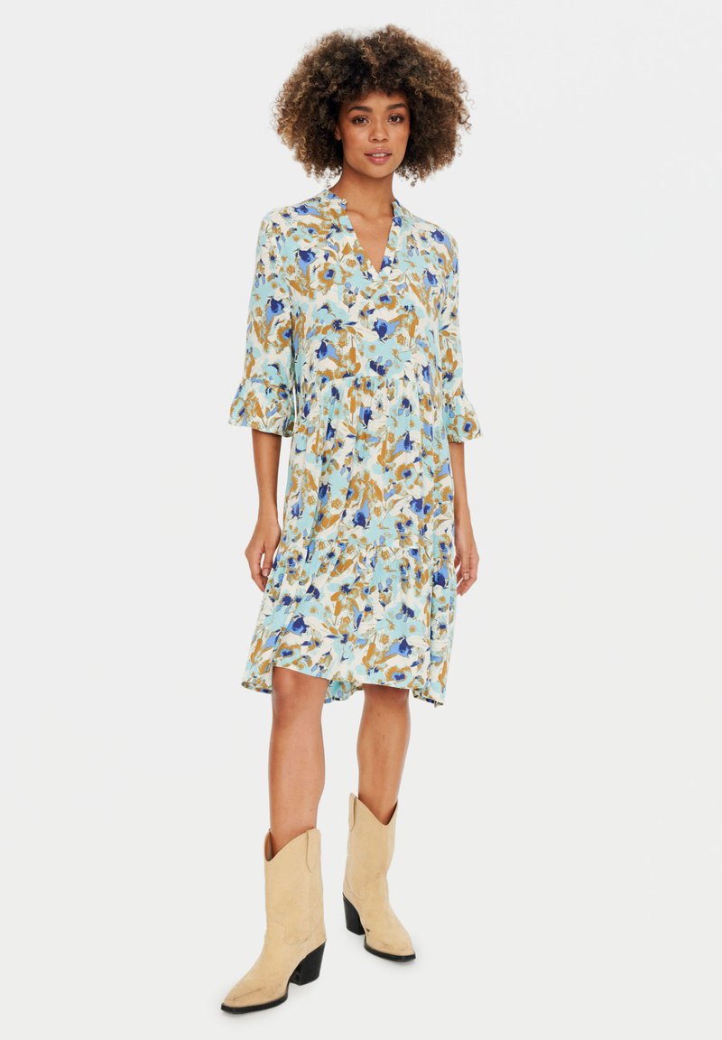 Rochie florală albastră cu mâneci trei sferturi, decolteu în V și un design în straturi. Purtați cu cizme cowboy maronii. Materialul este ușor și cu un model.