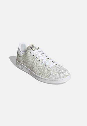 Weißer Adidas Low-Top-Sneaker mit Schnürung vorne und dezentem Animal-Print-Muster am Obermaterial, Ansicht von der rechten Seite und vorne.
