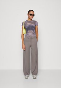 Fitted tie-dye top in gray and blue tones, paired with light gray wide-leg trousers. Accessorized with a small yellow bag and sunglasses.