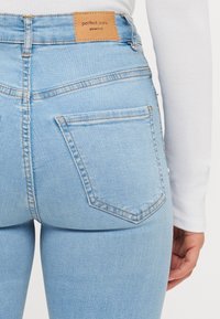 Ljusblå högmidjade jeans med en texturerad denimfinish. Har en beige läderetikett och två bakfickor med sömnadsdetaljer.