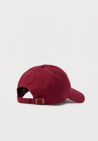 Κόκκινο βαμβακερό καπέλο μπέιζμπολ, με ρυθμιζόμενο λουρί στο πίσω μέρος, κυρτή γείσο και έξι οπές αερισμού. Η υφή του υφάσματος φαίνεται απαλή και ανθεκτική.